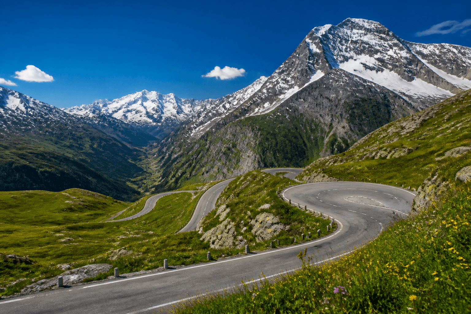 Alpine switchback road above meadows and snow peaks